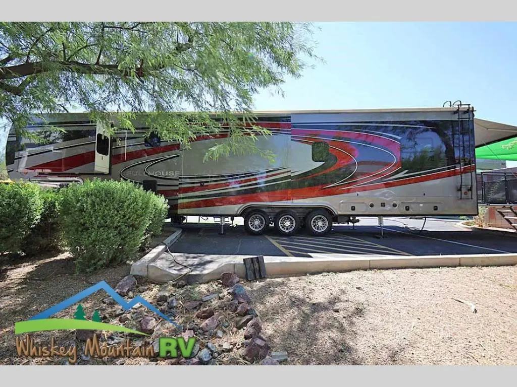 A large rv parked in the shade of a tree.